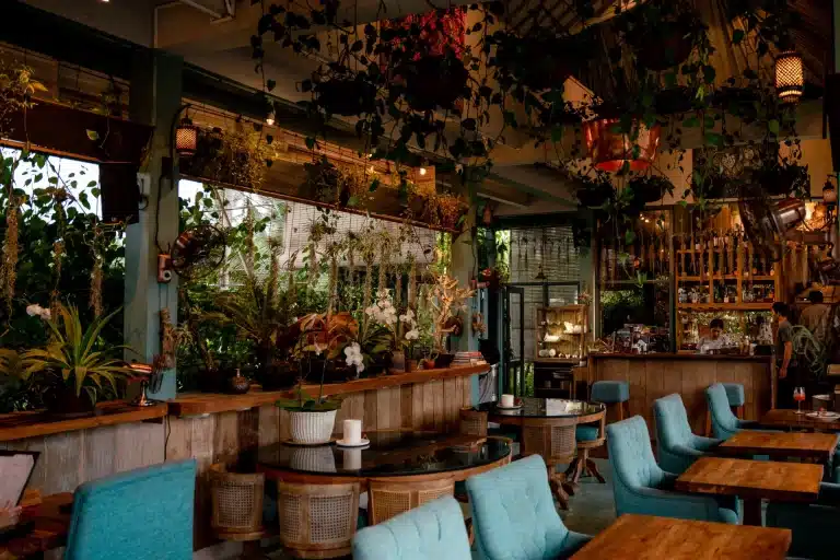 Muse garden bar with hanging plants, wooden tables and teal chairs