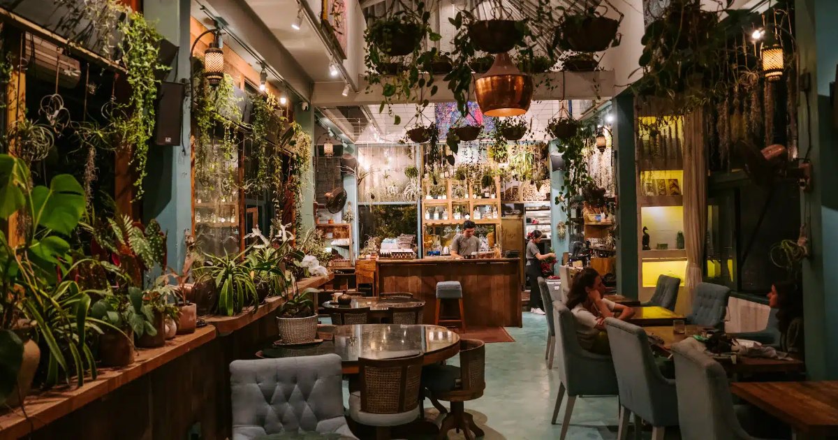 Evening at Muse Café & Art in Ubud: cascading plants, a tufted armchair and marble tables, with the bar glowing behind